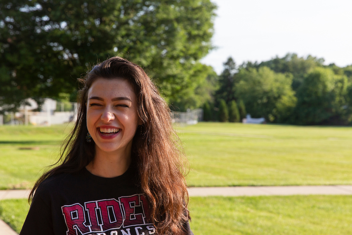 Student smiles for photo on campus green.