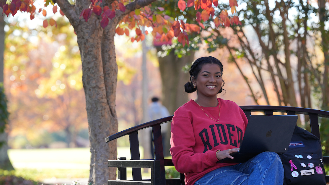 Rider student sitting on bench with laptop