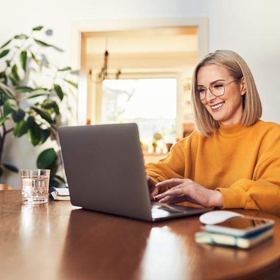Woman sits at table smiling while looking at computer