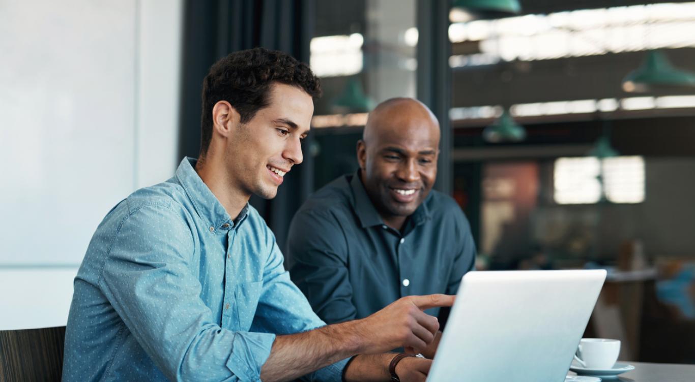 Two men sit at table and look at computer